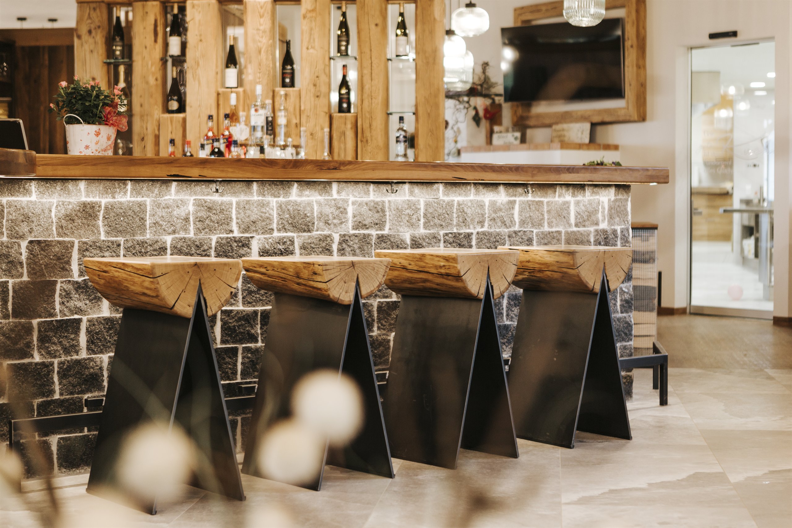 Bar mit Natursteinwand und Hockern aus Altholz